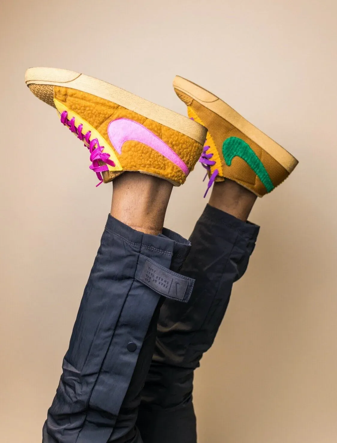 Two colorful sneakers held up against a tan wall