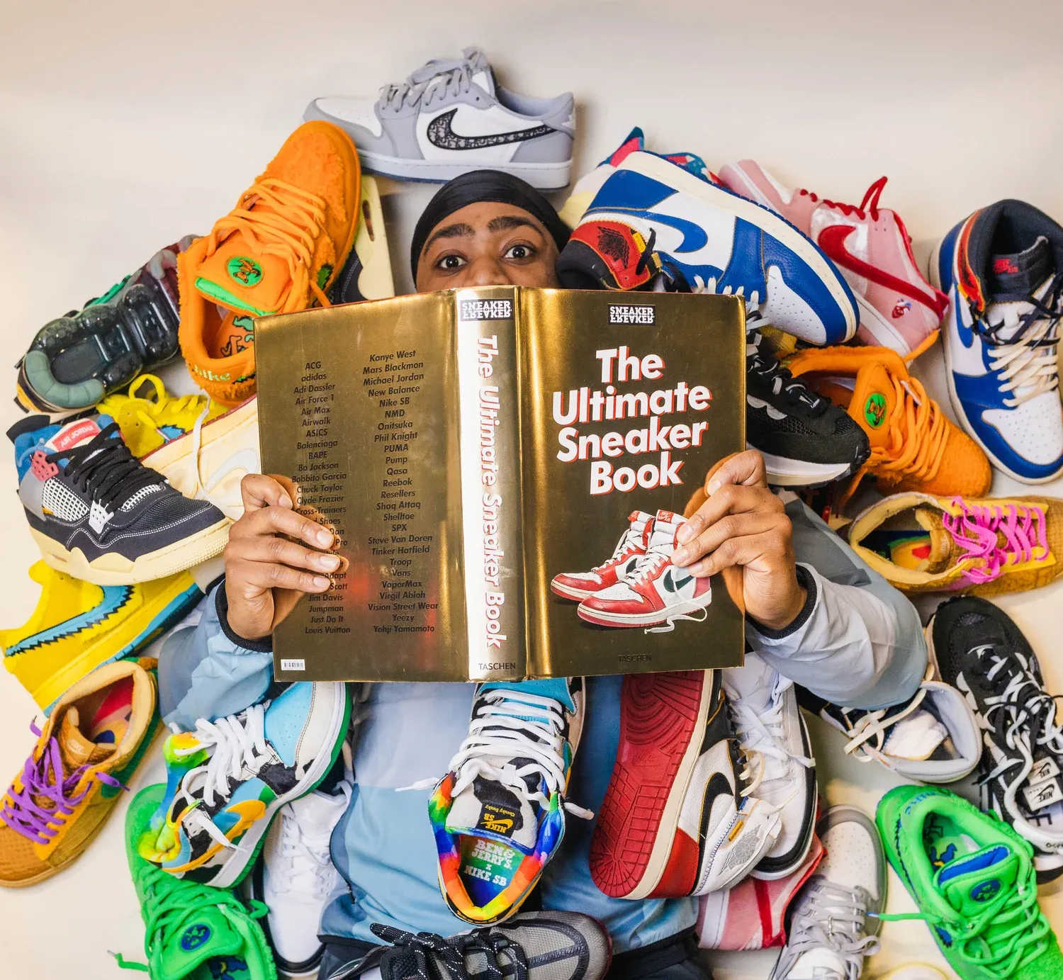 Kelechi reading The Ultimate Sneaker Book surrounded by sneakers